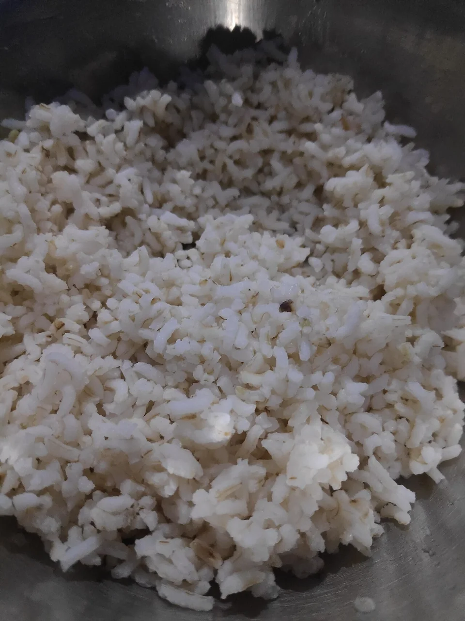 A metal bowl is filled with cooked white rice grains.