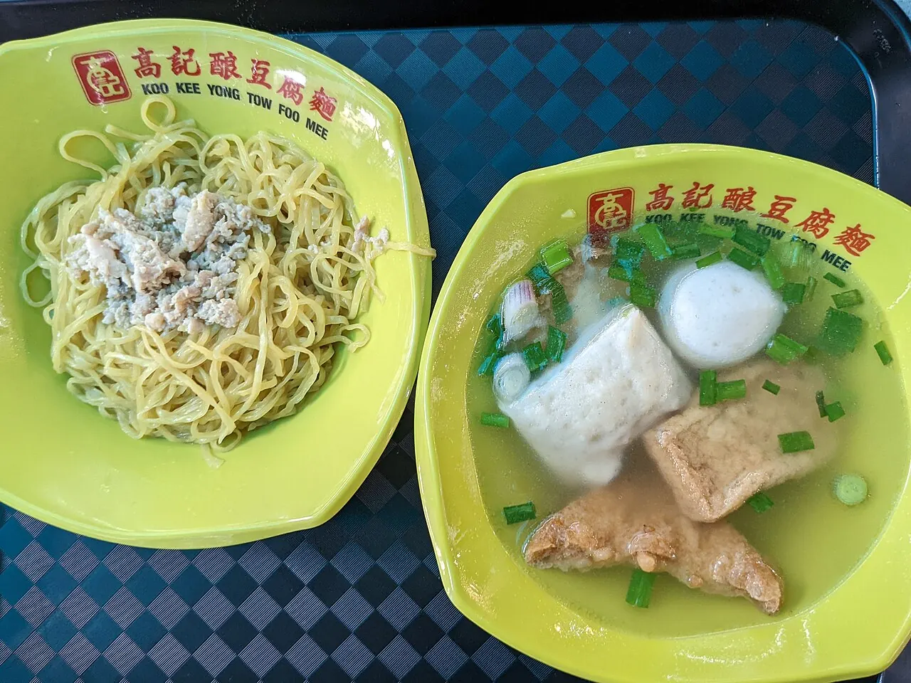 Two yellow plates show noodles with minced pork and a clear soup with tofu, fishball and stuffed bean curd pieces.