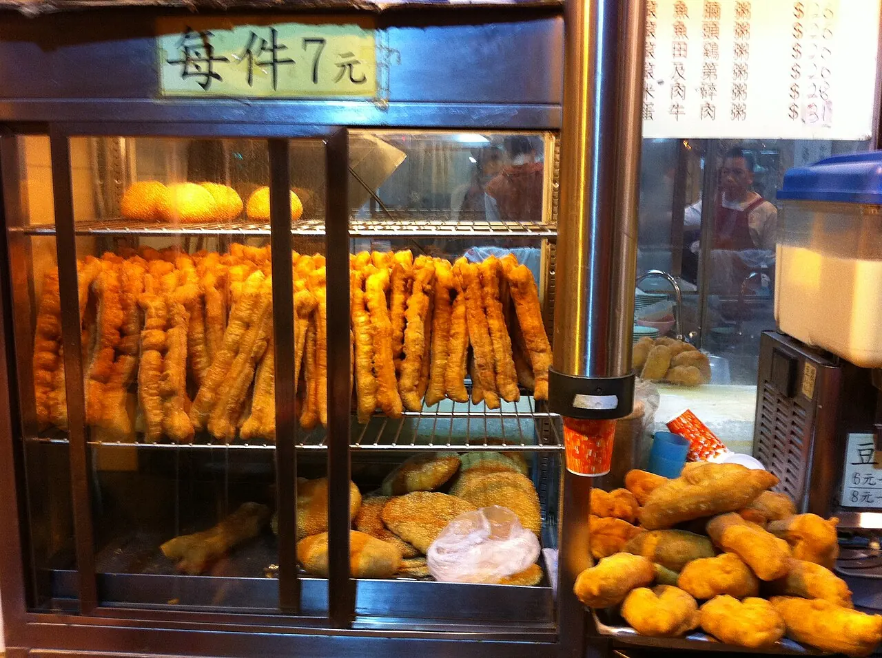 Rows of golden you tiao are stacked on shelves inside a glass display case at a shop.
