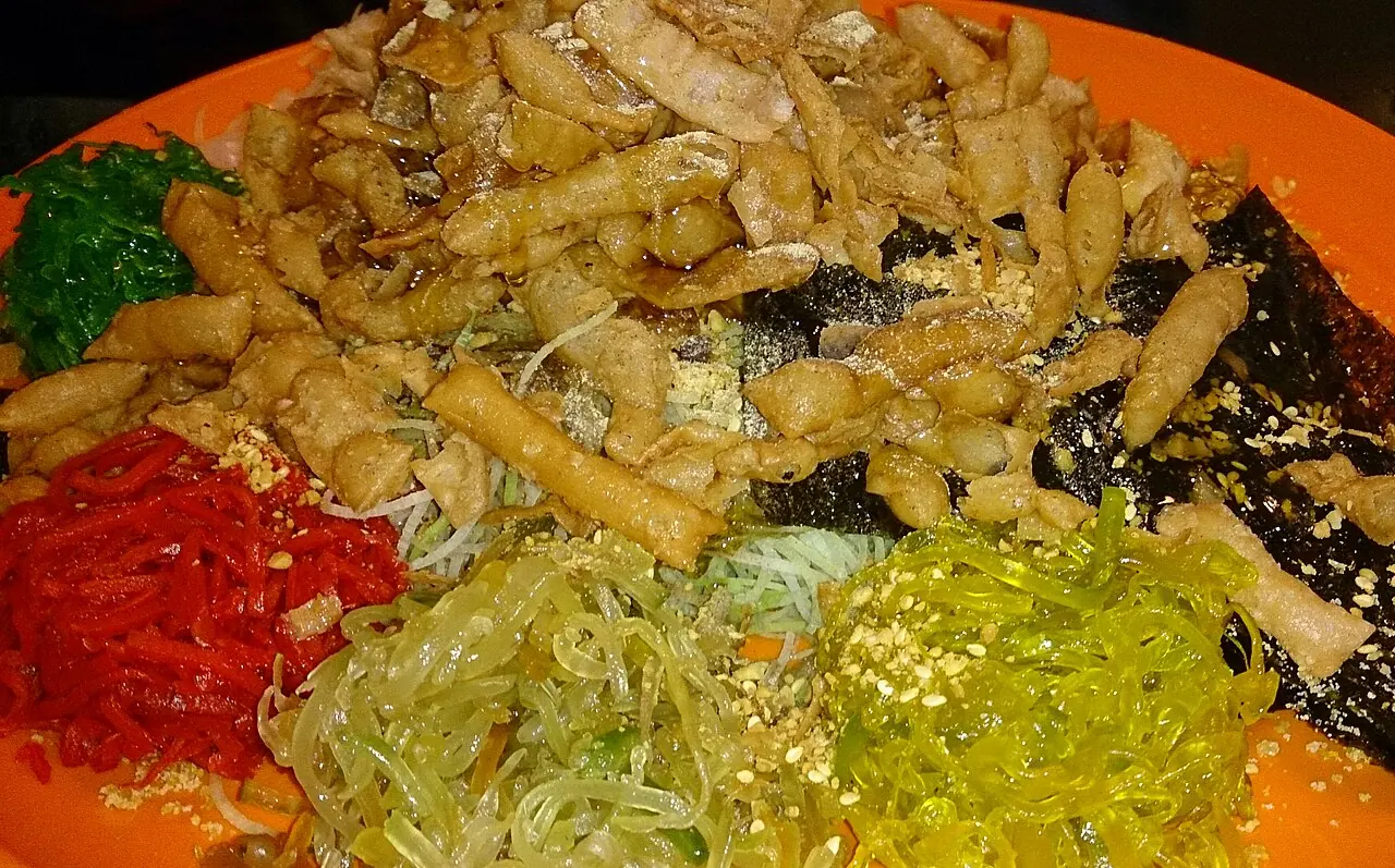 A plate of yu sheng topped with shredded vegetables, crisps, and sauces.