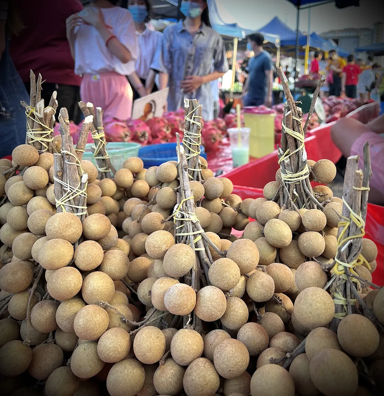 Longan — Bunches of brown longans piled at a market stall.