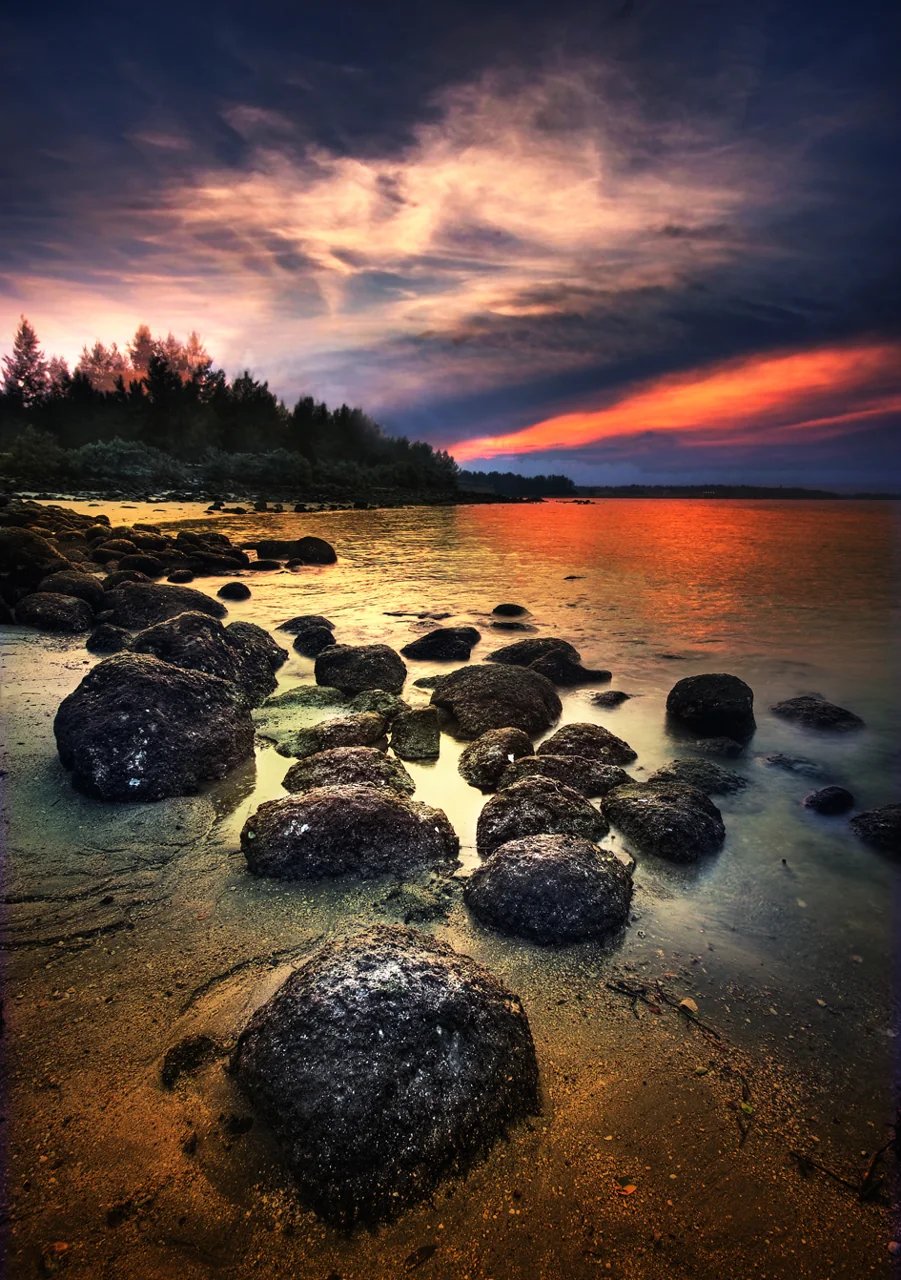 Rounded rocks sit on the wet sand at Punggol Beach beneath a colourful sunset.