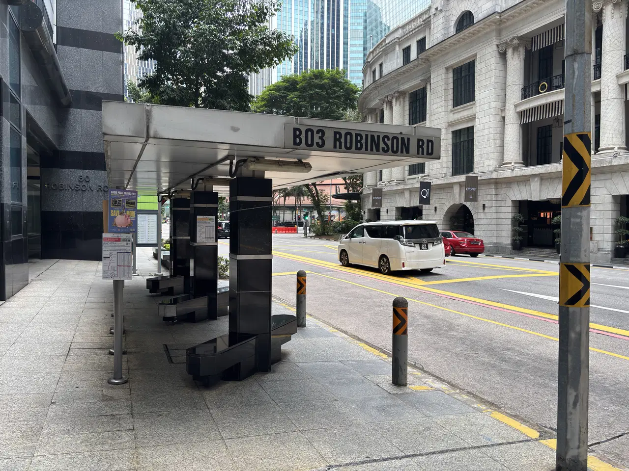 The covered B03 Robinson Road bus stop has seats and a route board beside the street.