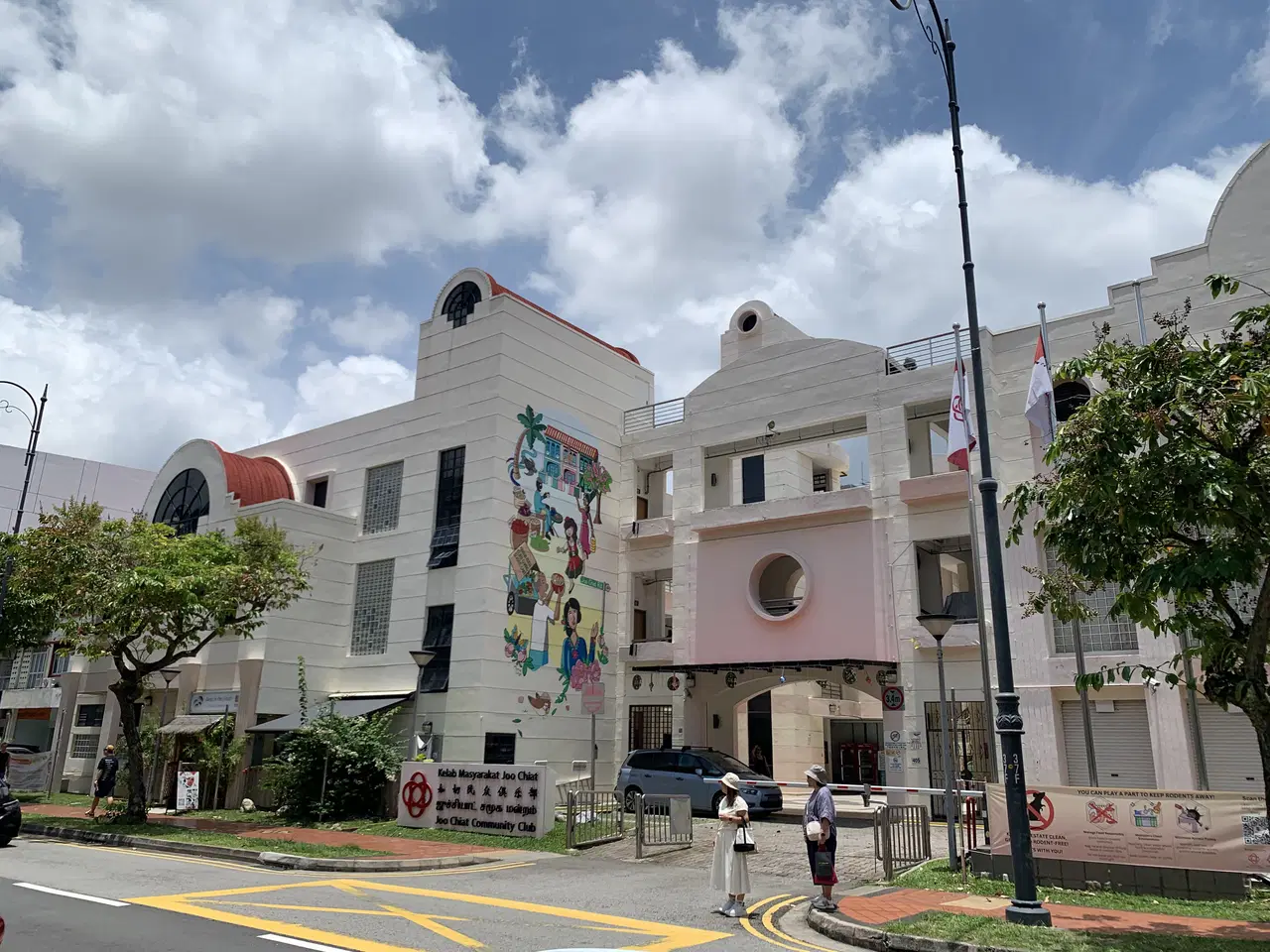 A pale community-club building has colourful murals beside a junction.