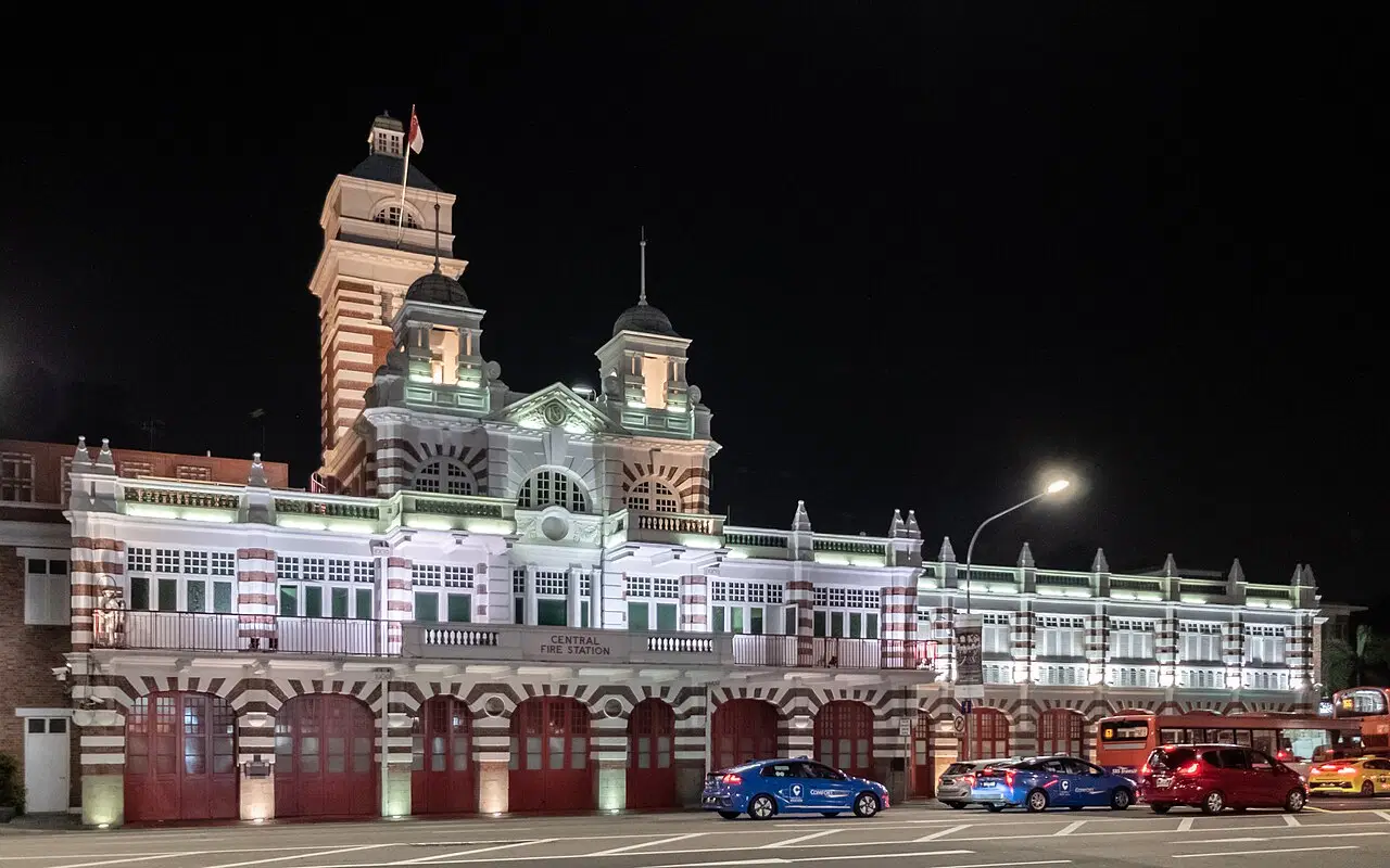 Singapore Central Fire Station glows at night behind passing cars.