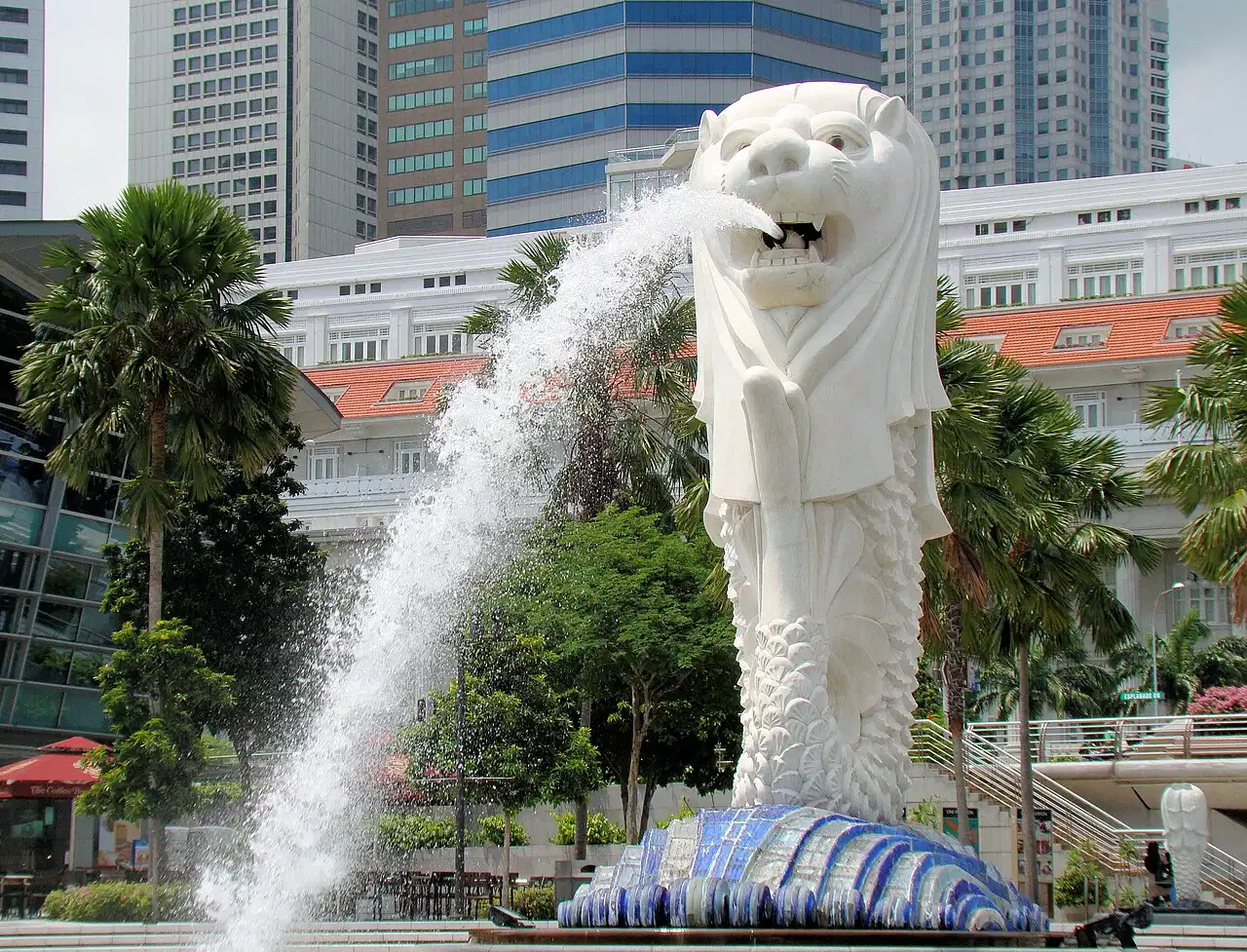 Water sprays from the Merlion fountain with tall buildings behind it.