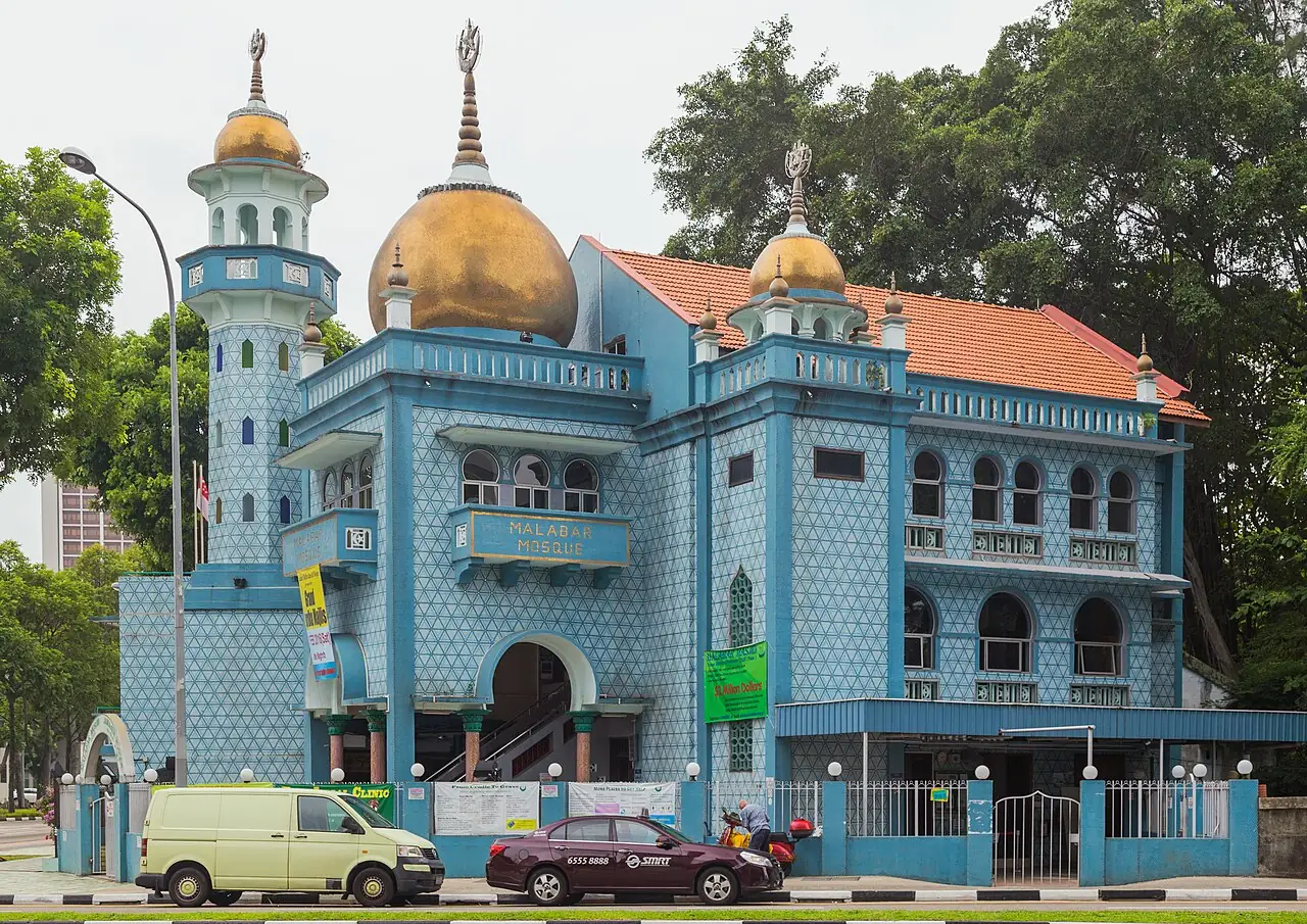 A blue mosque with golden domes stands beside a Kampong Glam street.