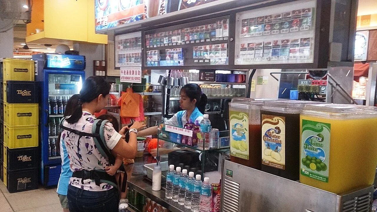 A customer stands at a drinks counter with drink dispensers and menu boards.