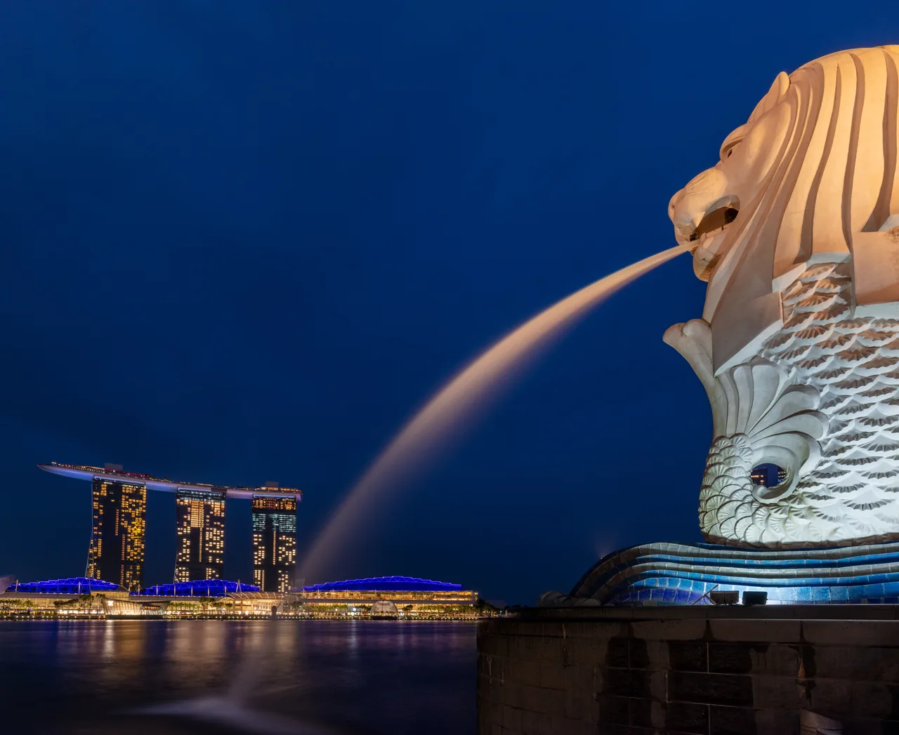 The Merlion statue sprays water beside the bay at dusk.