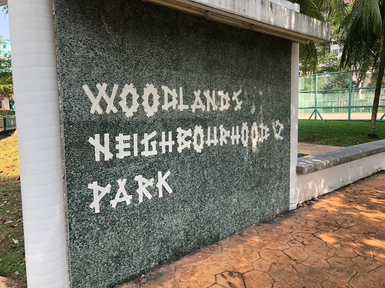 A stone park sign sits beside grass and trees.