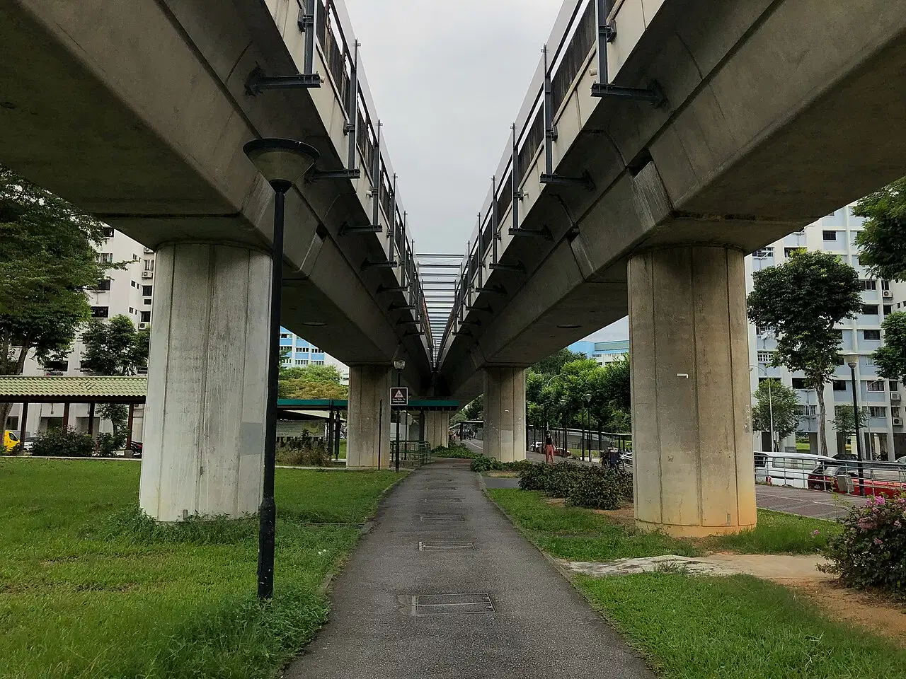 A paved path runs beneath two concrete viaducts through grass.