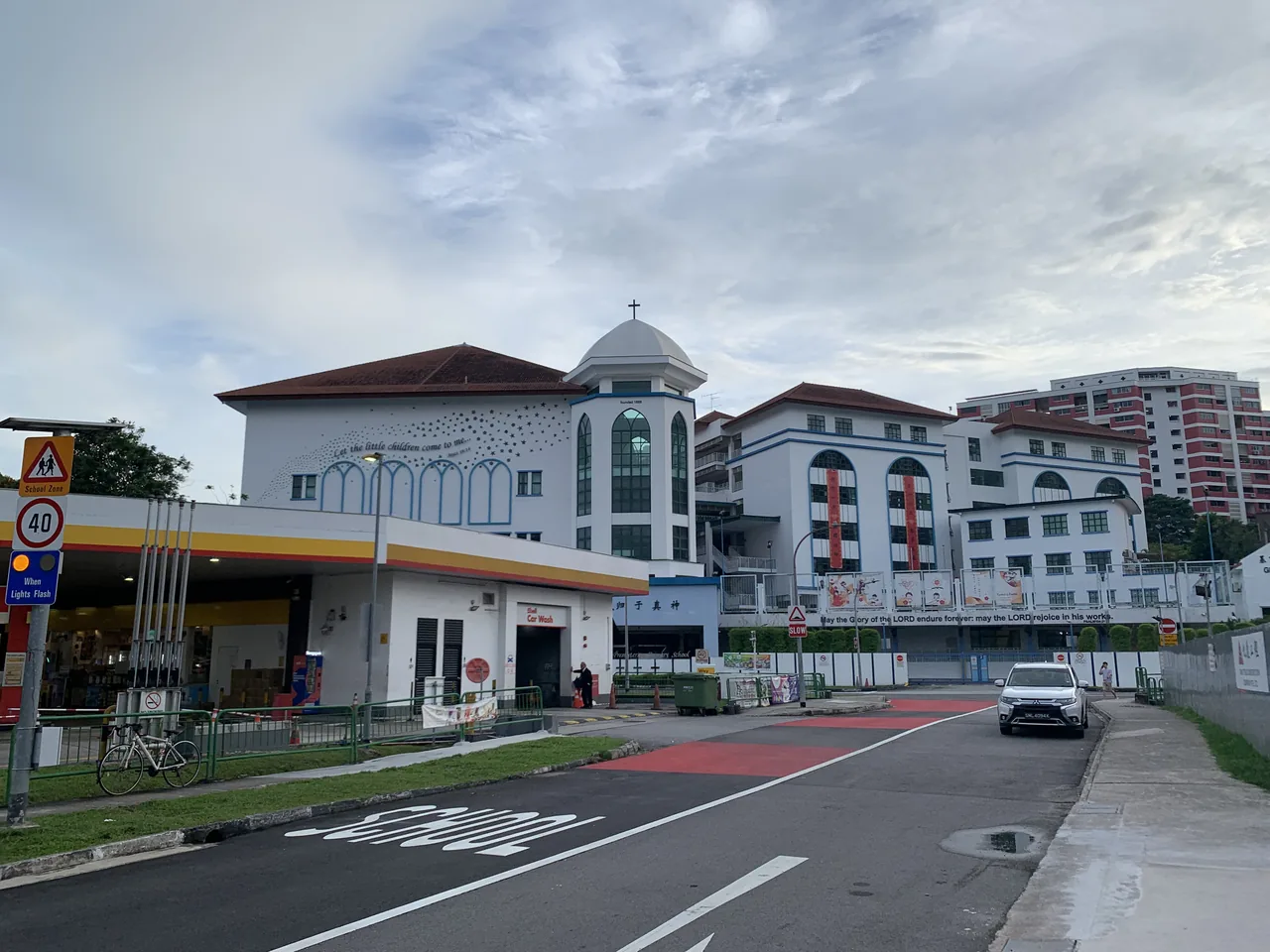 A school entrance and white buildings sit beyond a quiet road.