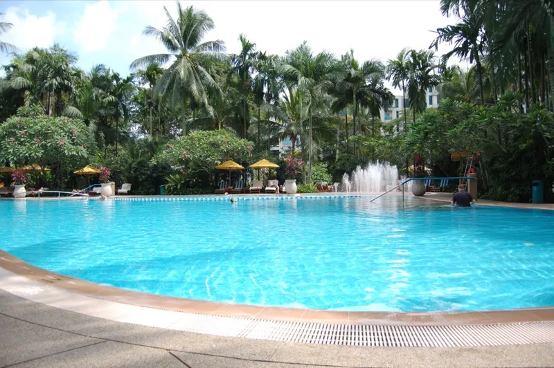 A blue hotel pool sits among palms and a small waterfall.