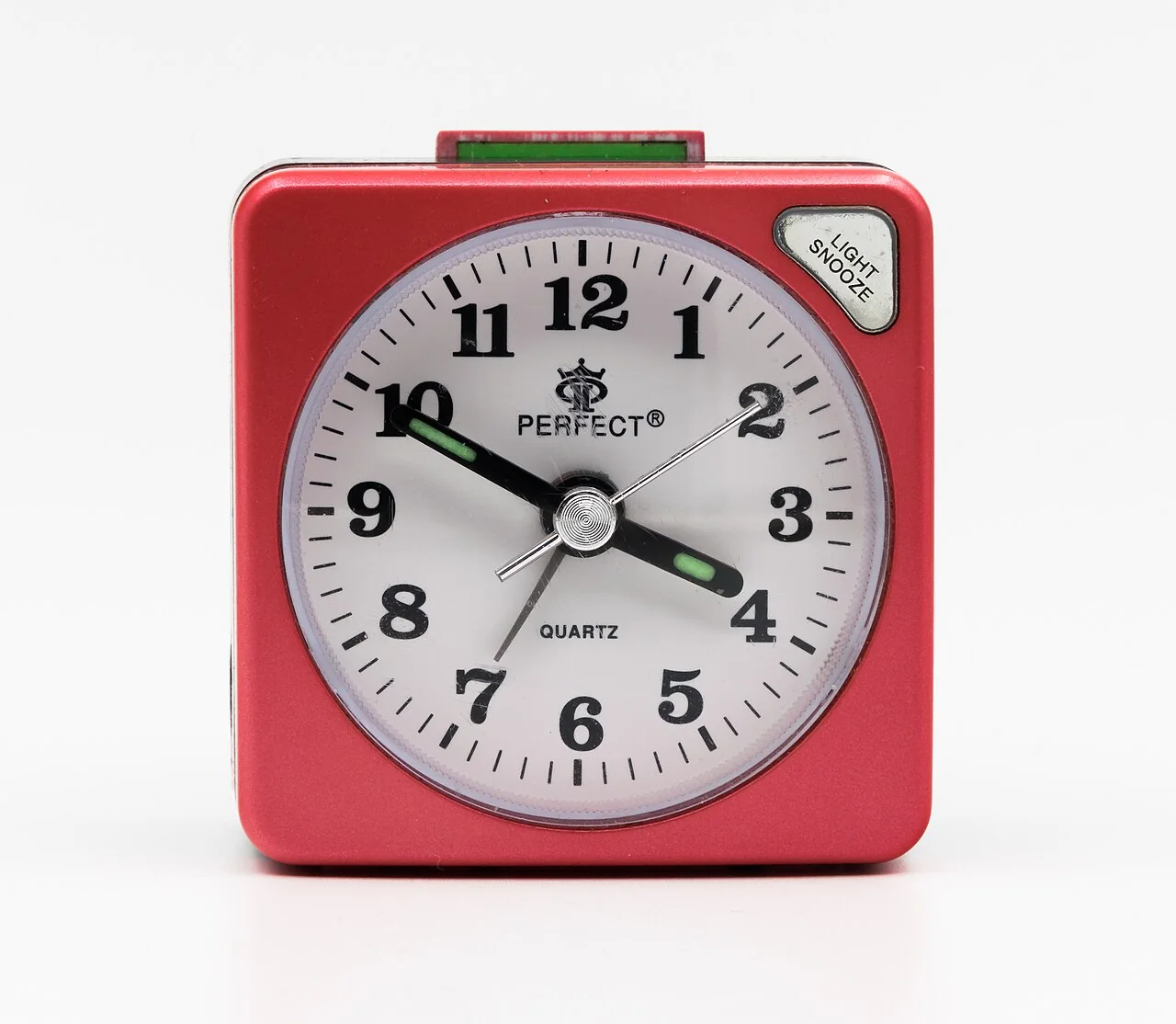 A red square Perfect quartz alarm clock with a white dial and black numerals sits on a white surface.