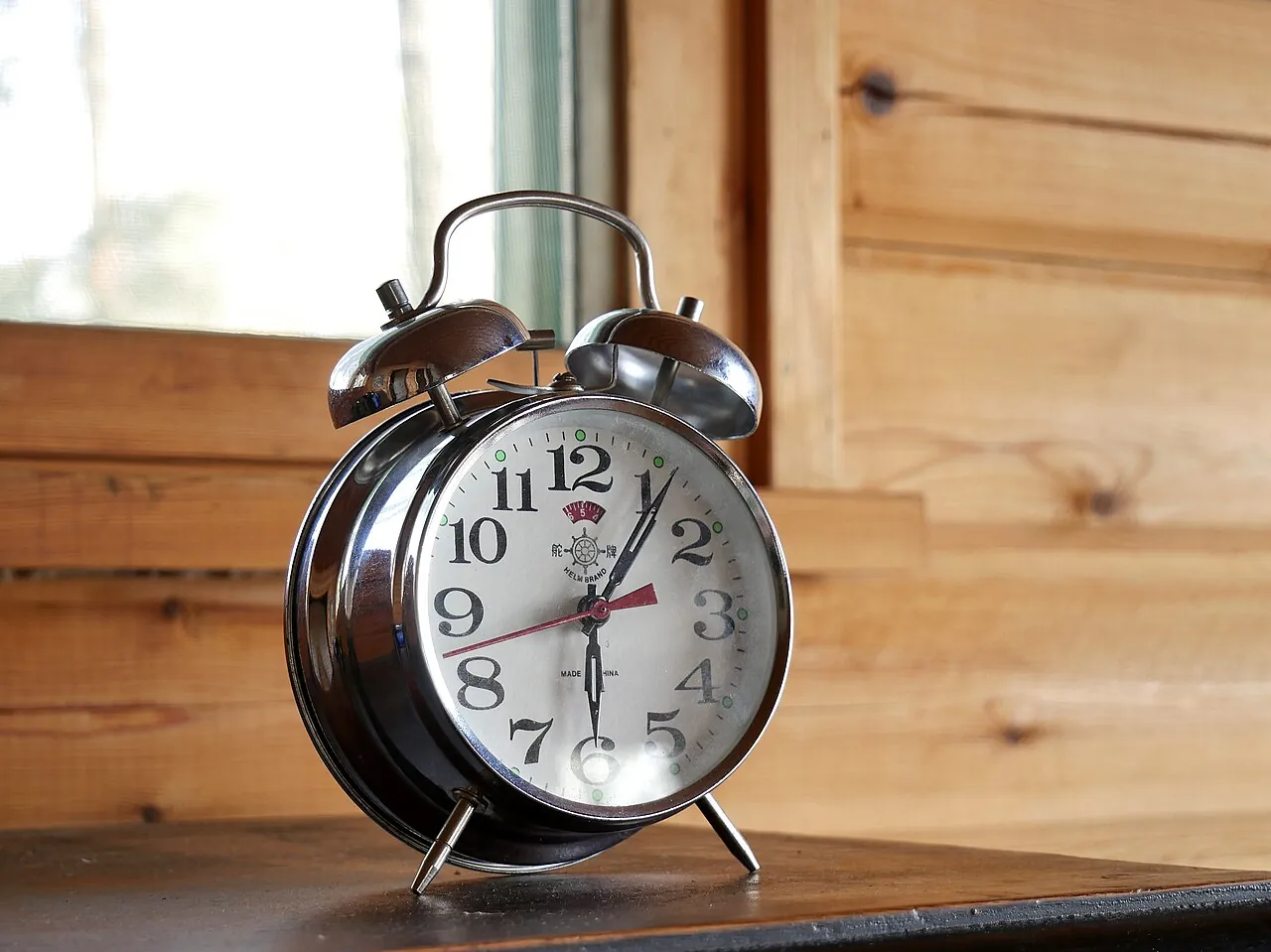 A silver alarm clock sits on a wooden shelf.