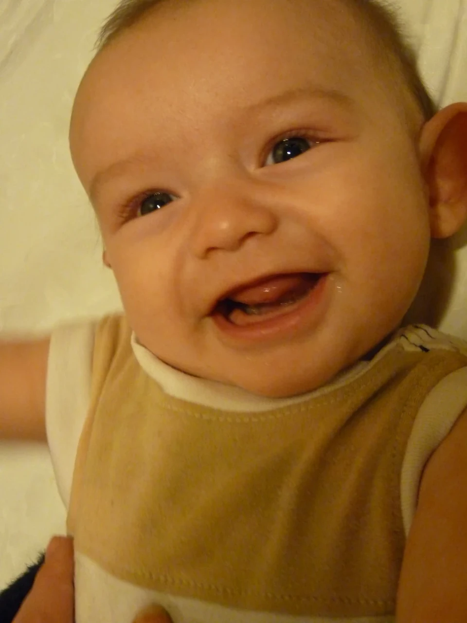 A smiling baby wears a pale yellow bib, with an open mouth and bright eyes.