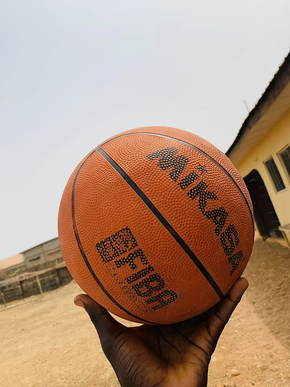 A hand holds an orange basketball with black curved lines.