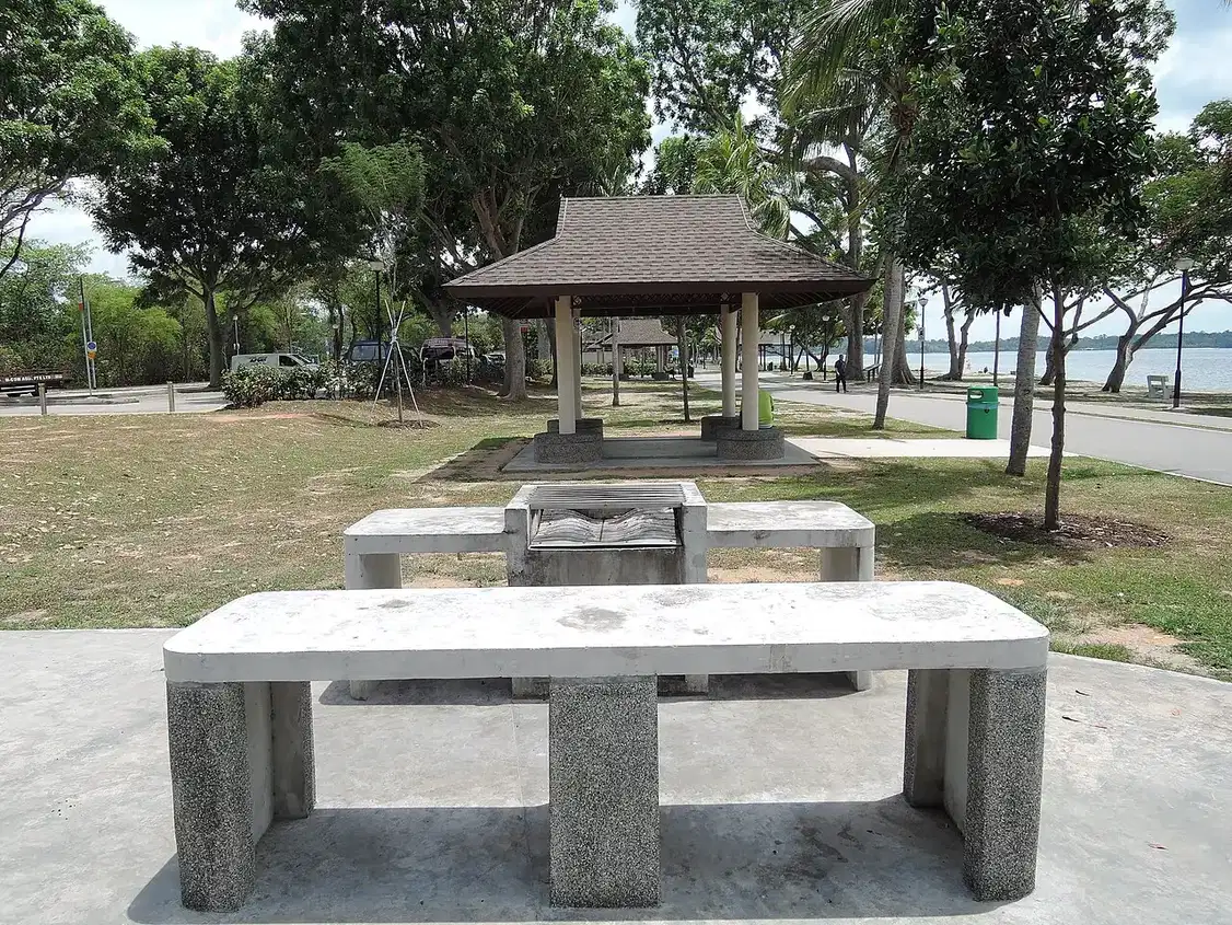 Concrete barbecue pits and benches beside a park pavilion.