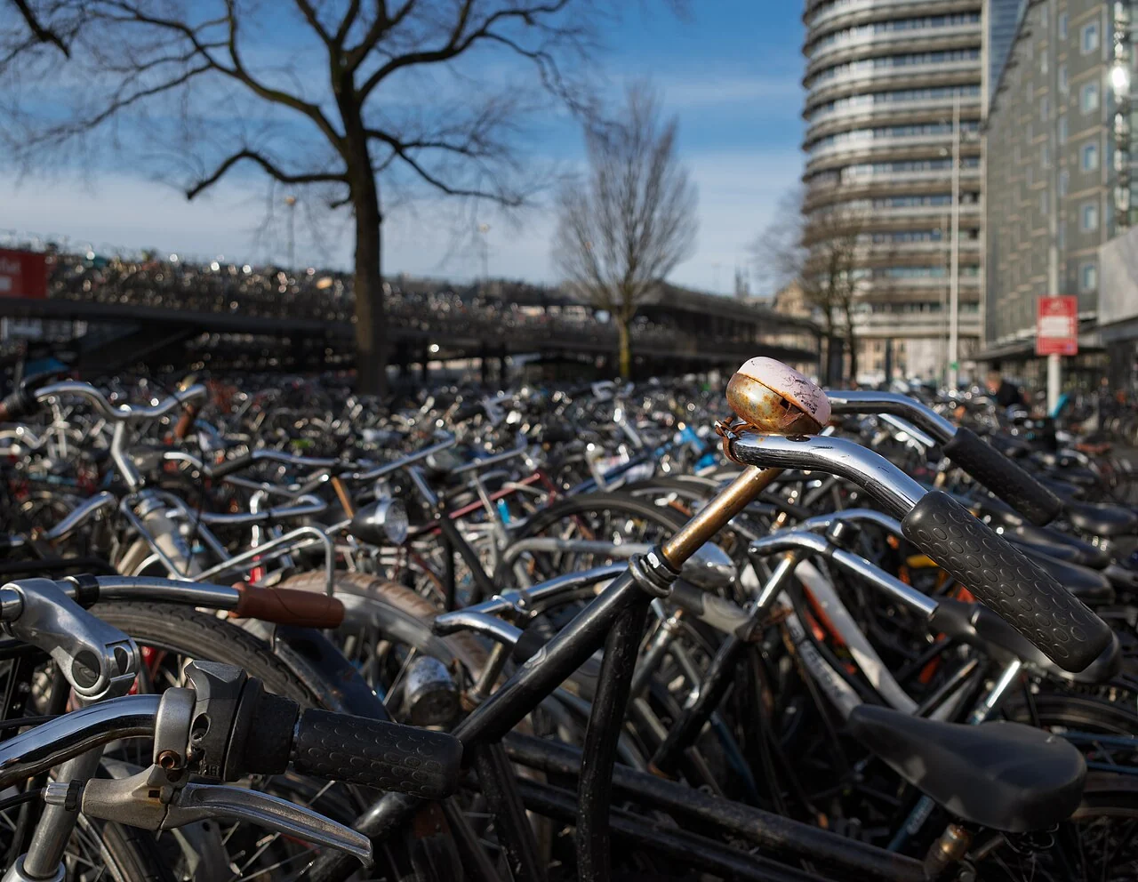 A round metal bell sits on a bicycle handlebar above rows of parked bicycles.
