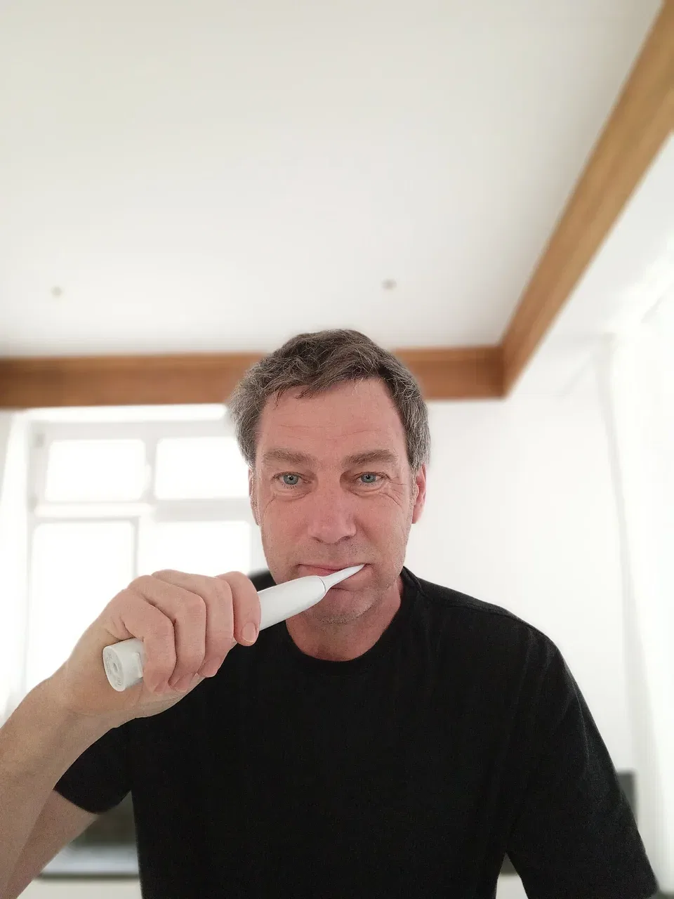 A man brushing his teeth with a white electric toothbrush.