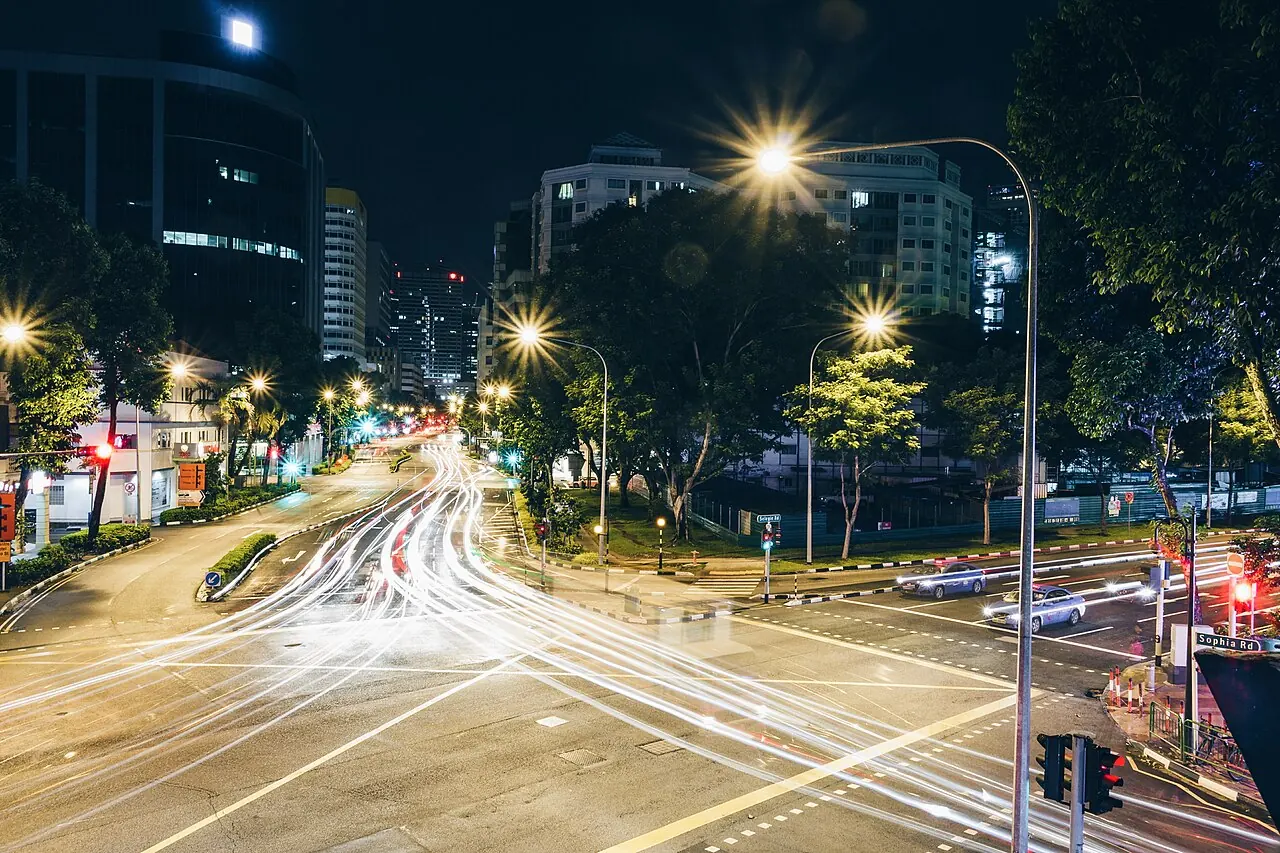 Long streaks of vehicle lights cross a wide city intersection at night.
