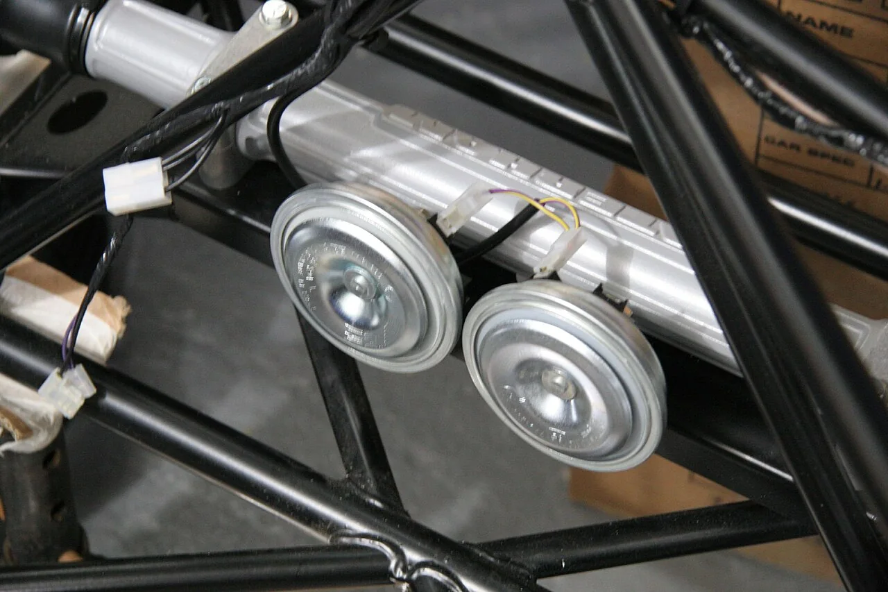 Two silver car horns are mounted on a black tubular frame.
