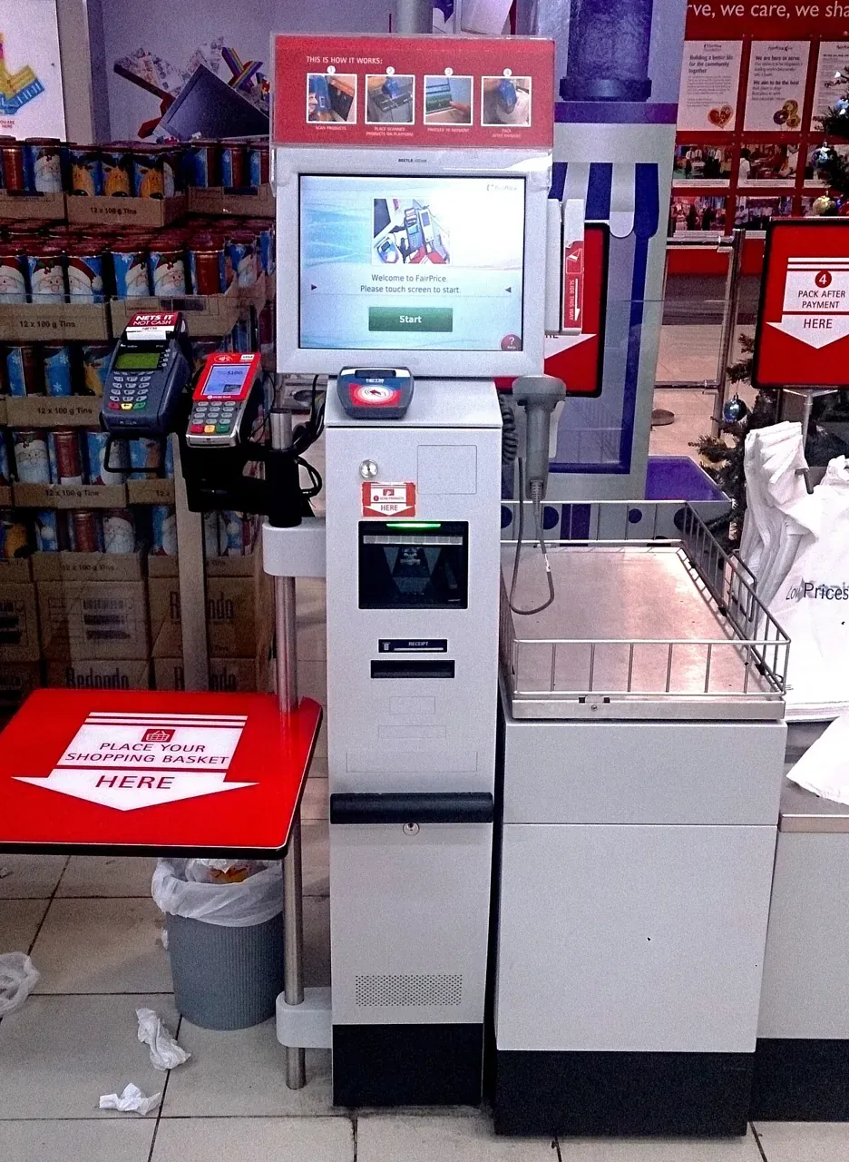 A self-checkout machine with a touchscreen and card reader stands in a supermarket.