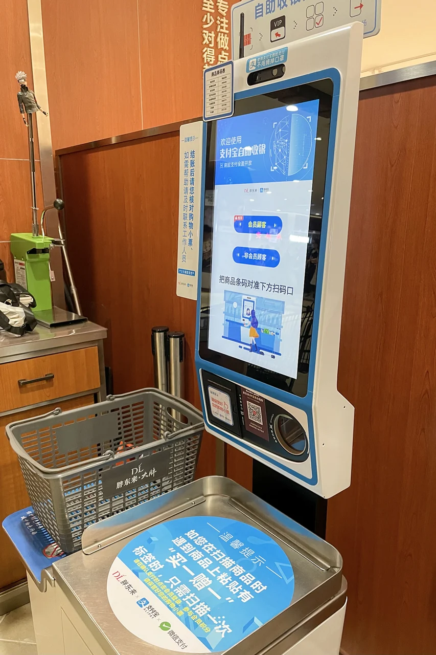 A self-checkout machine has a tall screen and a metal tray.
