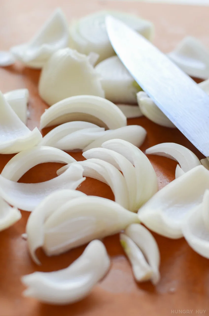 Sliced onions lie beside a knife on a wooden chopping board.