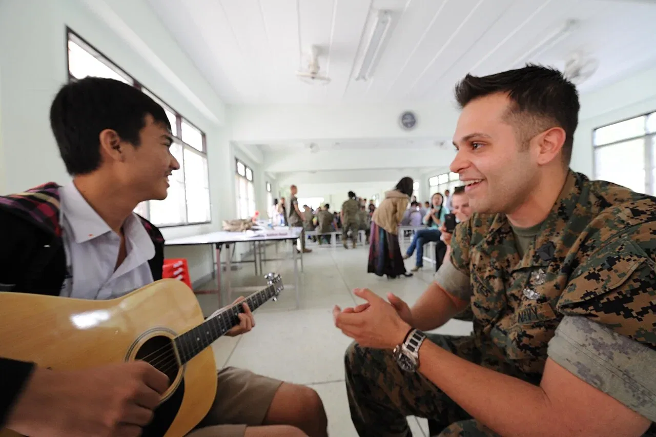 A man claps his hands beside a student playing guitar.