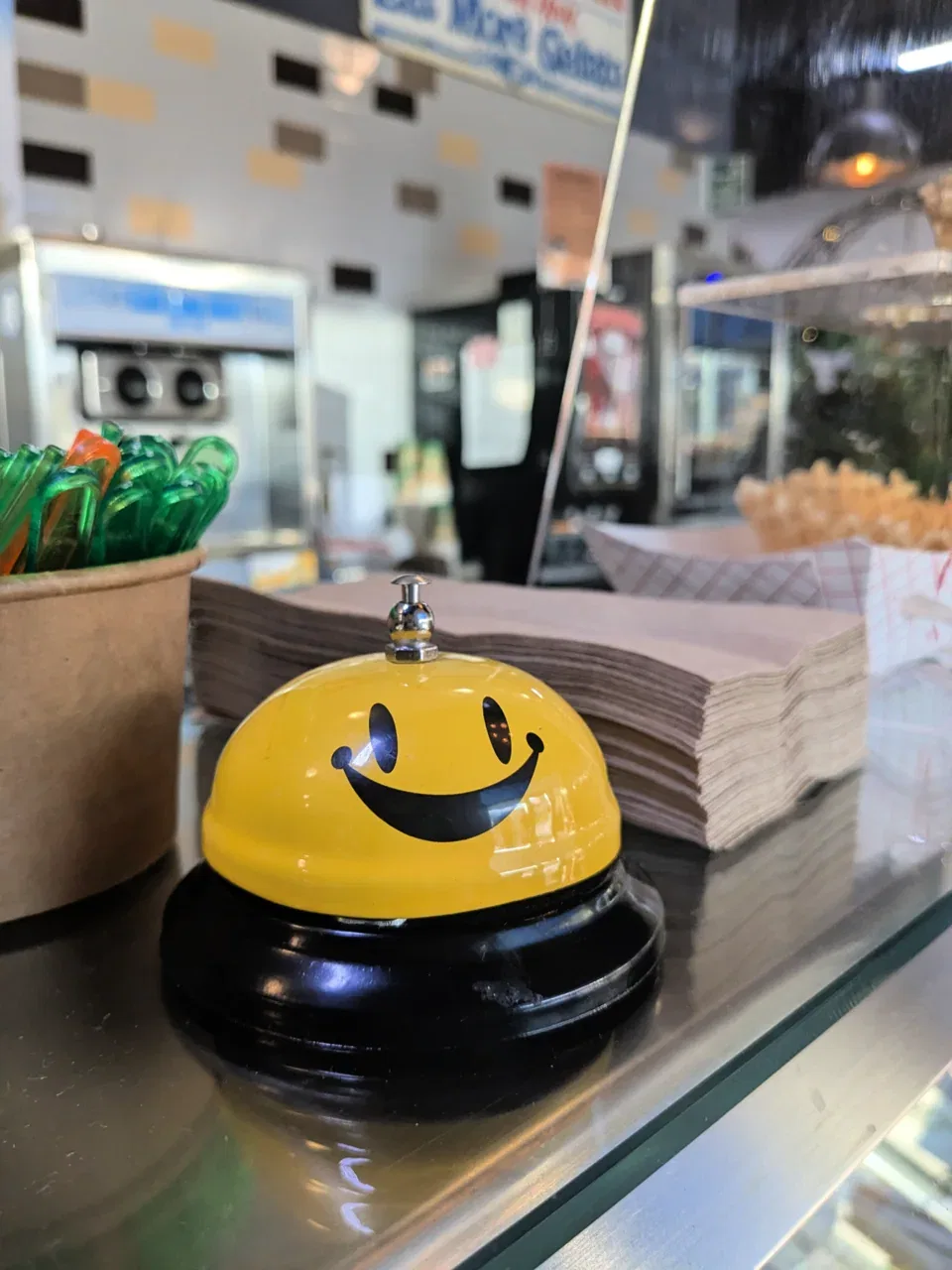 A yellow smiley-face service bell sits on a counter next to paper napkins.