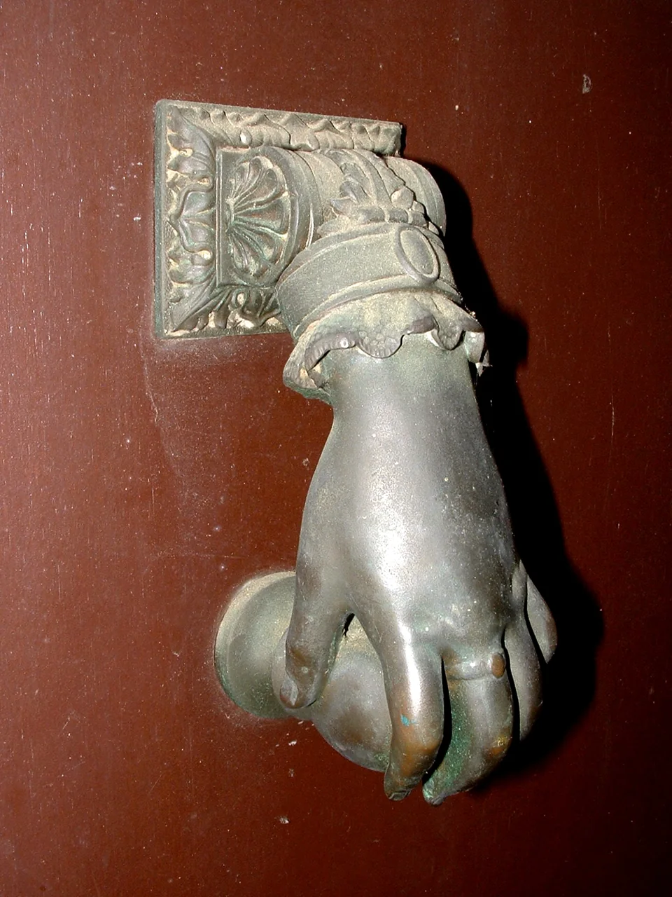 An ornate metal hand-shaped door knocker is attached to a red door.