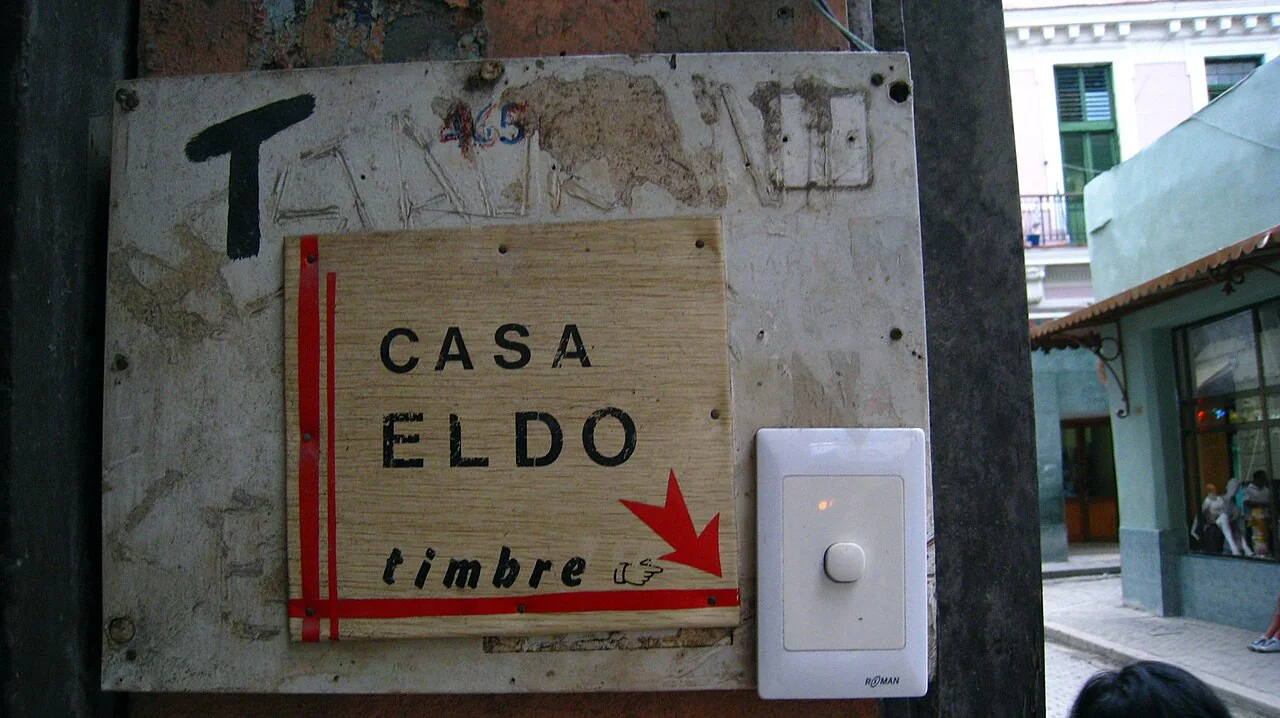 A white doorbell with a round button is mounted beside a wooden sign.