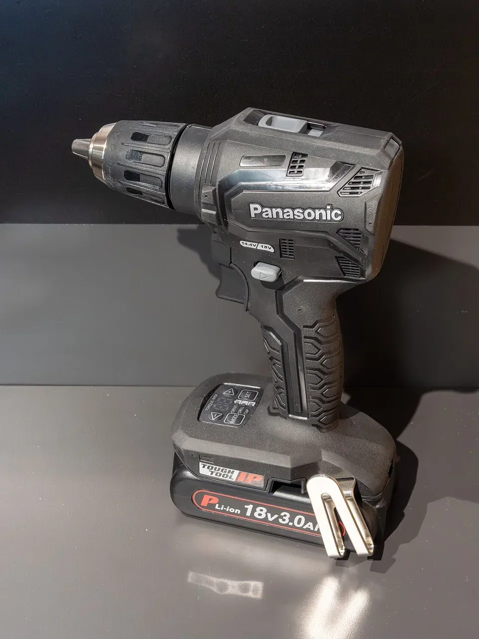 A black cordless drill stands on its battery on a dark surface.