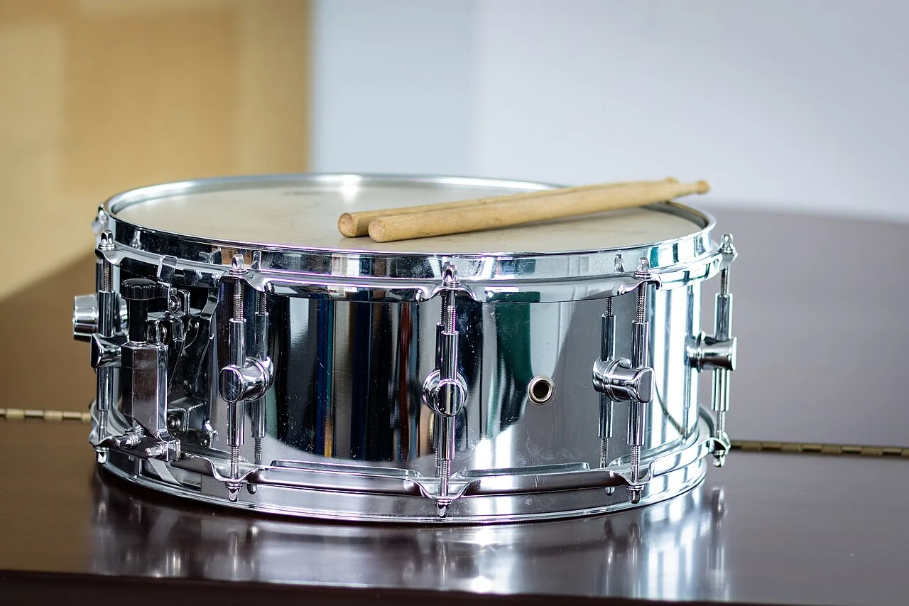 Two wooden drumsticks rest on the white top of a shiny drum.