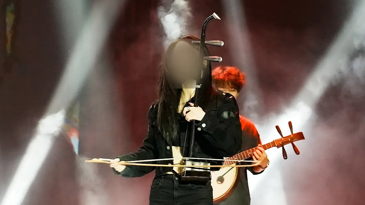 A musician plays an erhu under stage lights.