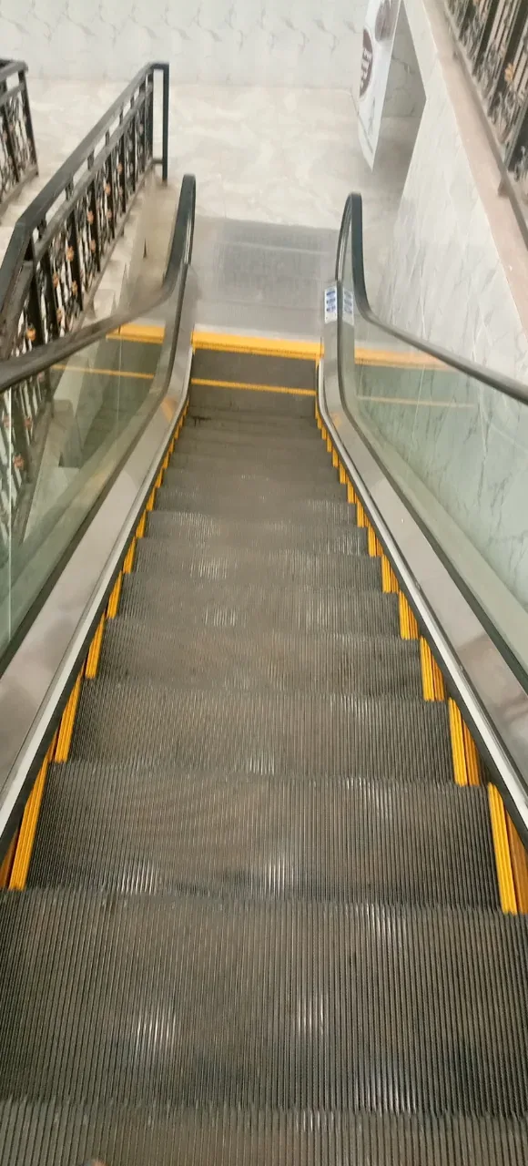 An empty escalator with yellow step edges descends between glass balustrades.