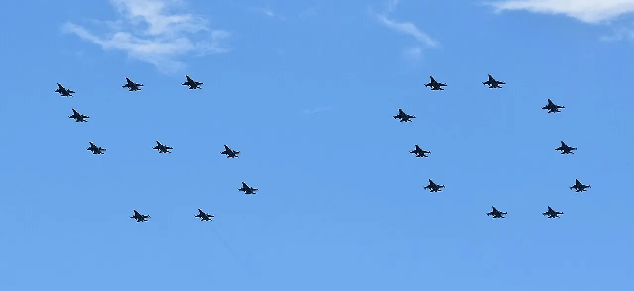 Many small jets fly in formation in a blue sky.