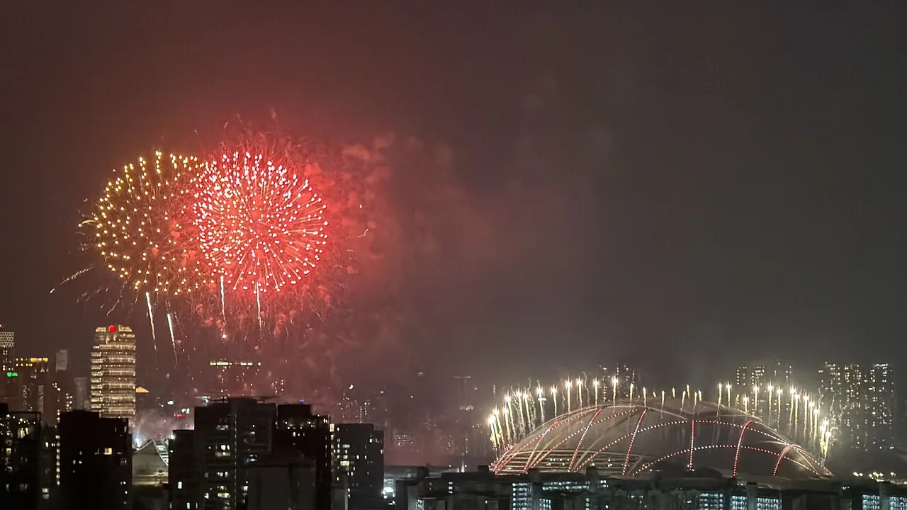 Red and gold fireworks burst in the night sky above city buildings and a domed structure.