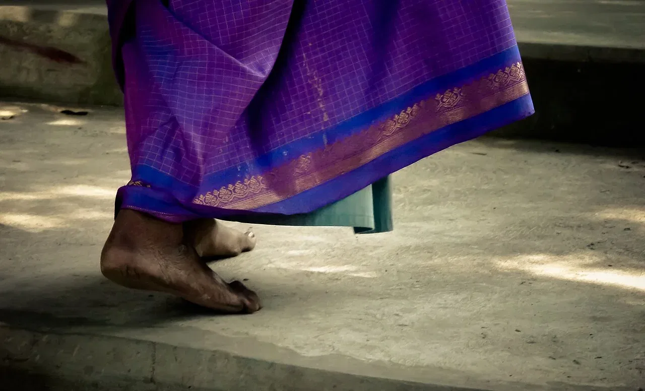 A person in a purple sari walks barefoot on a concrete surface.