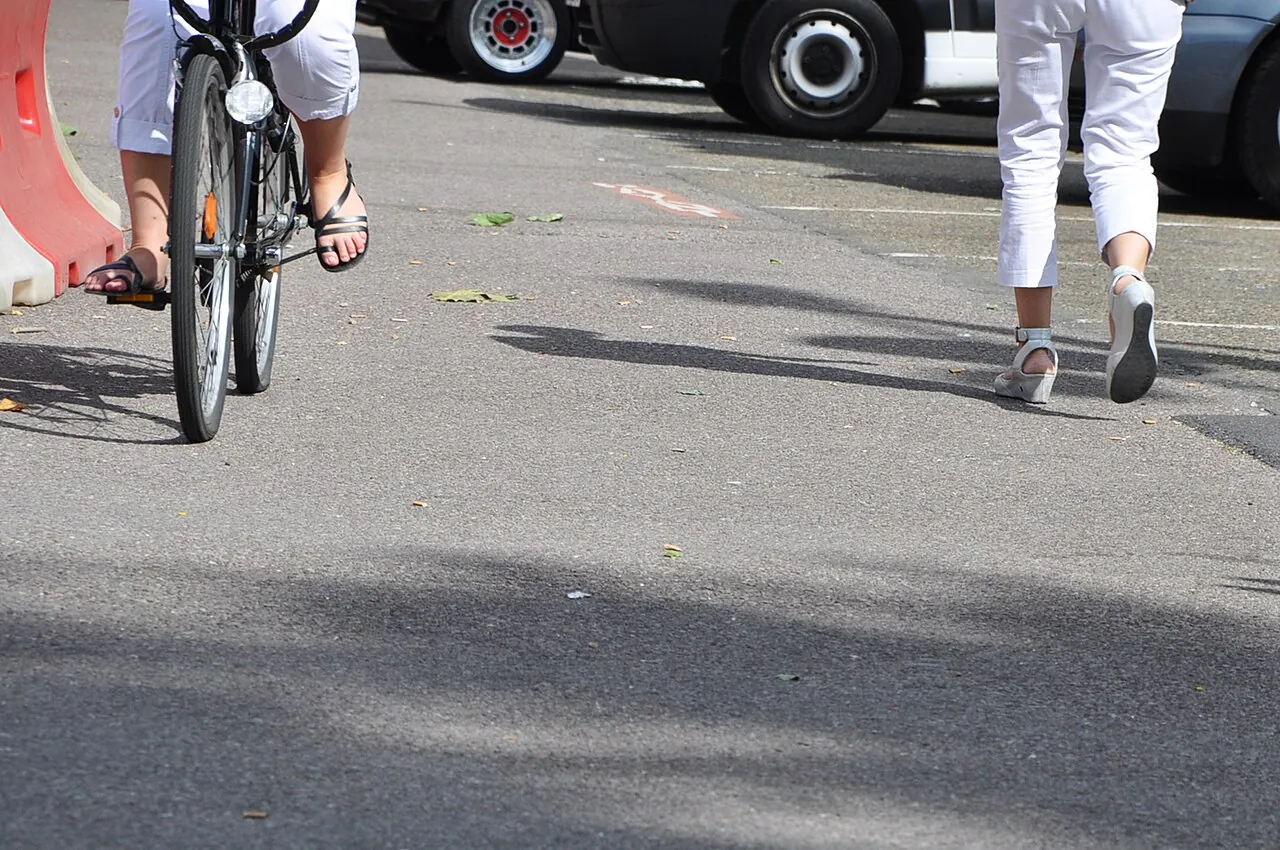 Feet and a bicycle wheel move along a road.