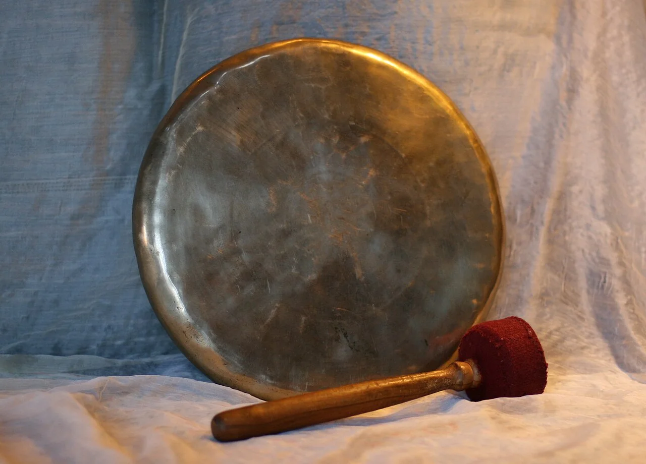 A round metal gong rests against a light blue cloth with a red-tipped mallet lying in front of it.