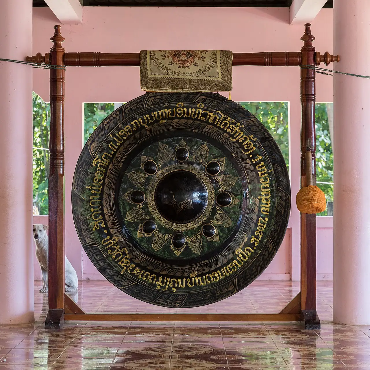 A large black gong with gold decorations hangs from a wooden frame inside a temple pavilion.