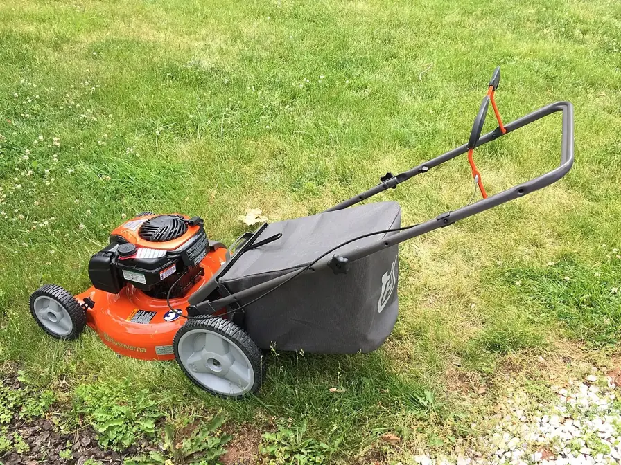 An orange lawn mower with a black grass bag sits on a lawn.