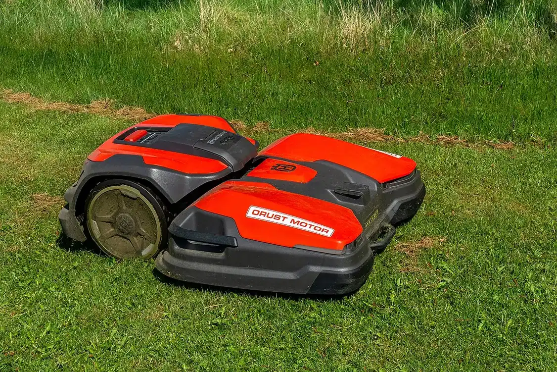 A red and black robotic lawn mower stands on green grass.