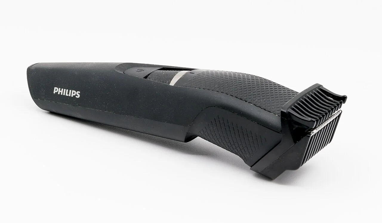 A black hair clipper with a comb guard lies on a white surface.