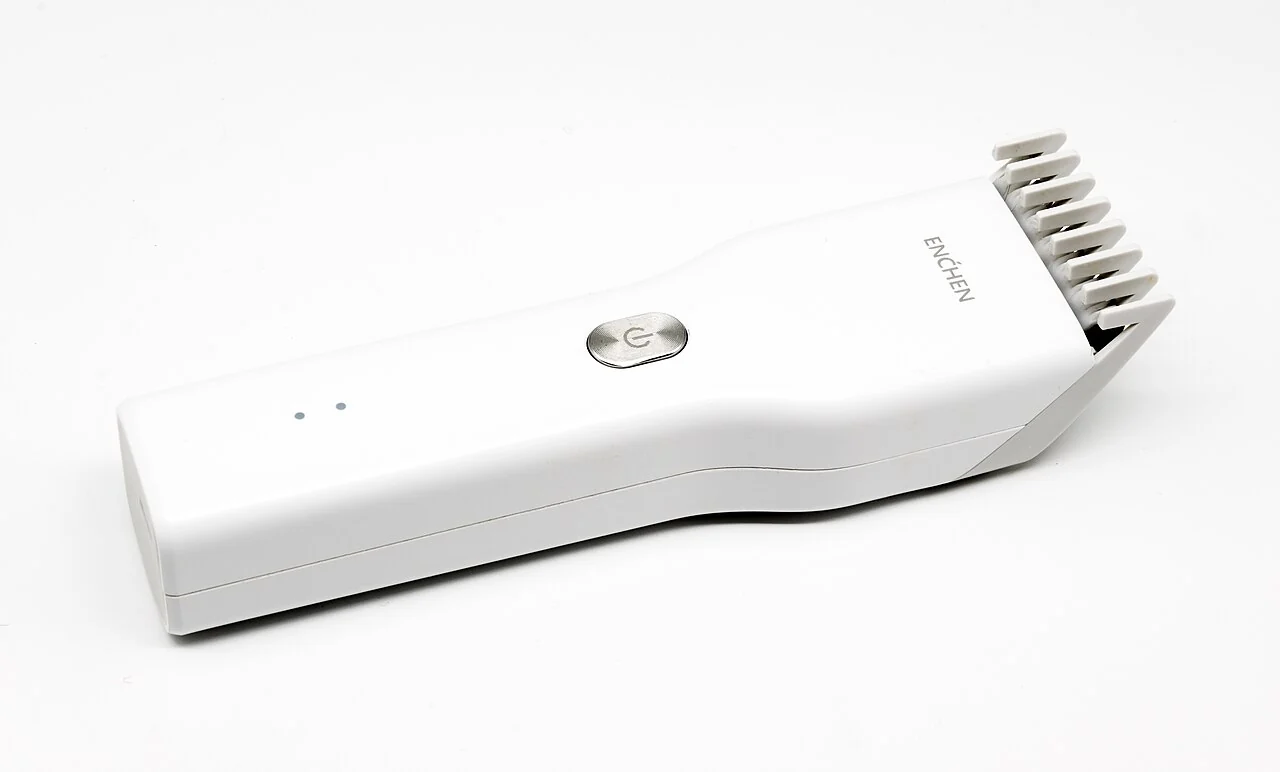 A white hair clipper has a comb attachment and a silver button.