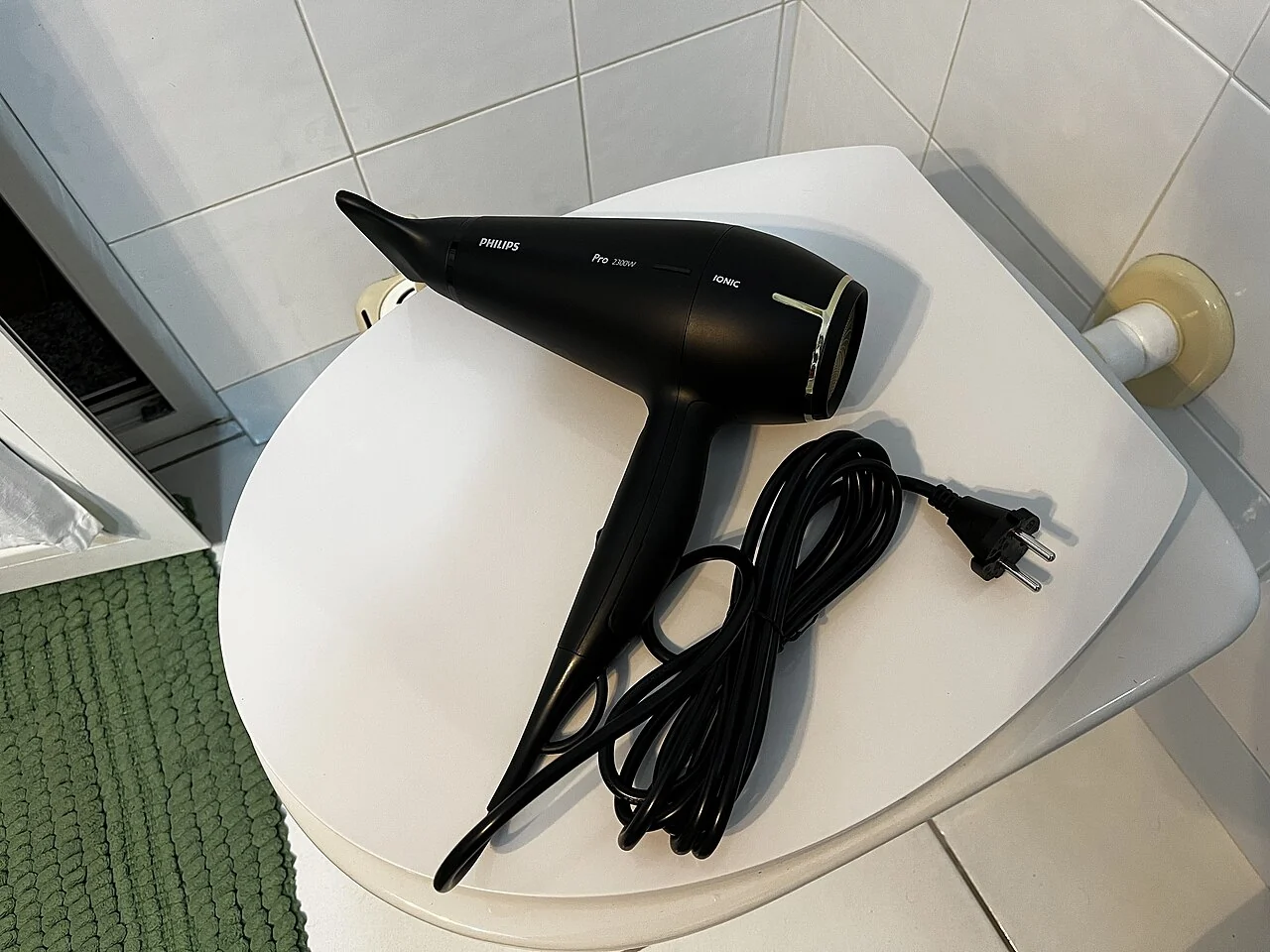 A black hair dryer lies beside its coiled cord and plug.