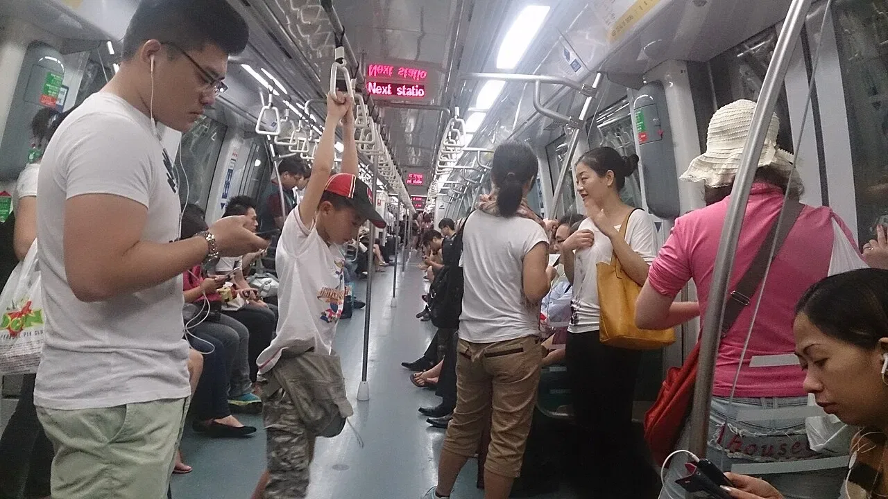 Passengers stand and sit inside a busy Singapore MRT carriage.