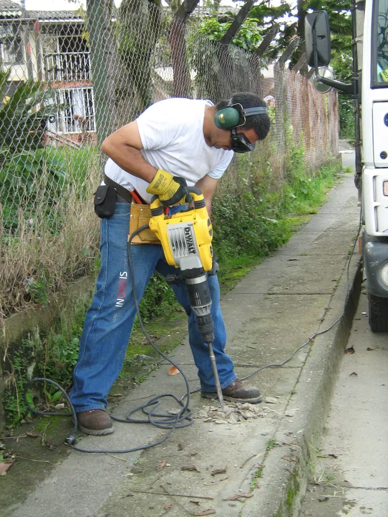 A person wearing ear protection uses a yellow jackhammer on a concrete pavement.